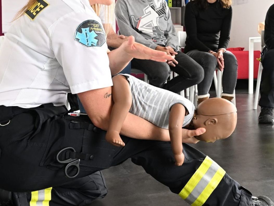 Un groupe de personnes est assis autour d'un ambulancier qui prodigue les premiers soins à un mannequin bébé.