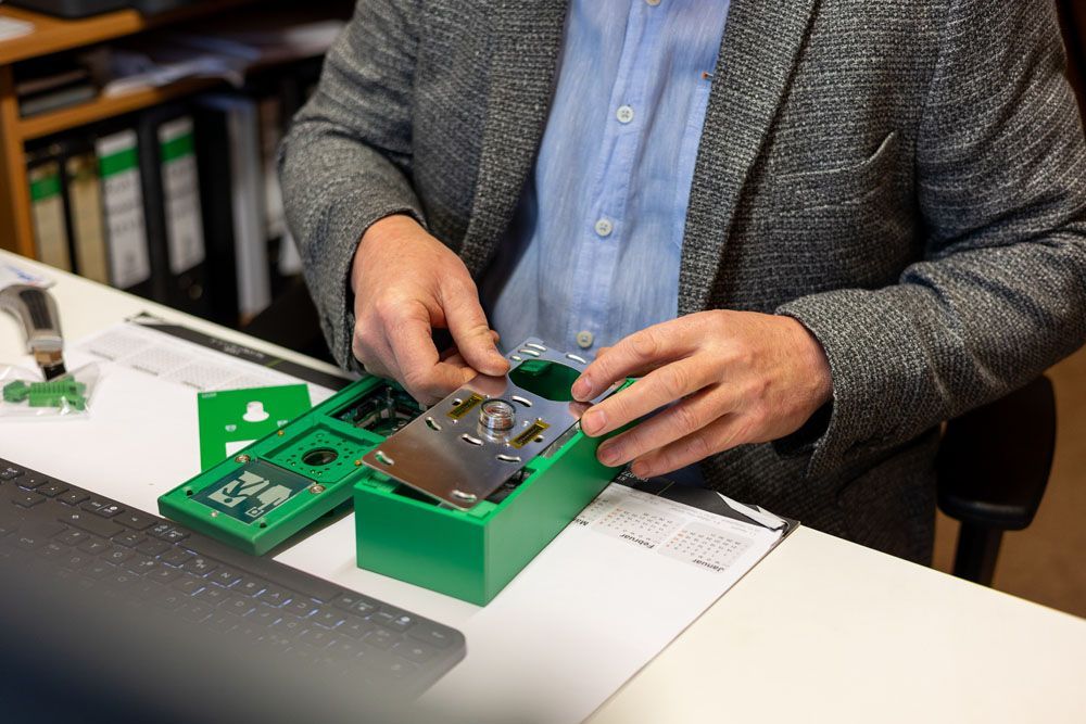 Ein Mann im Anzug sitzt an einem Schreibtisch und hält eine grüne Schachtel in der Hand.