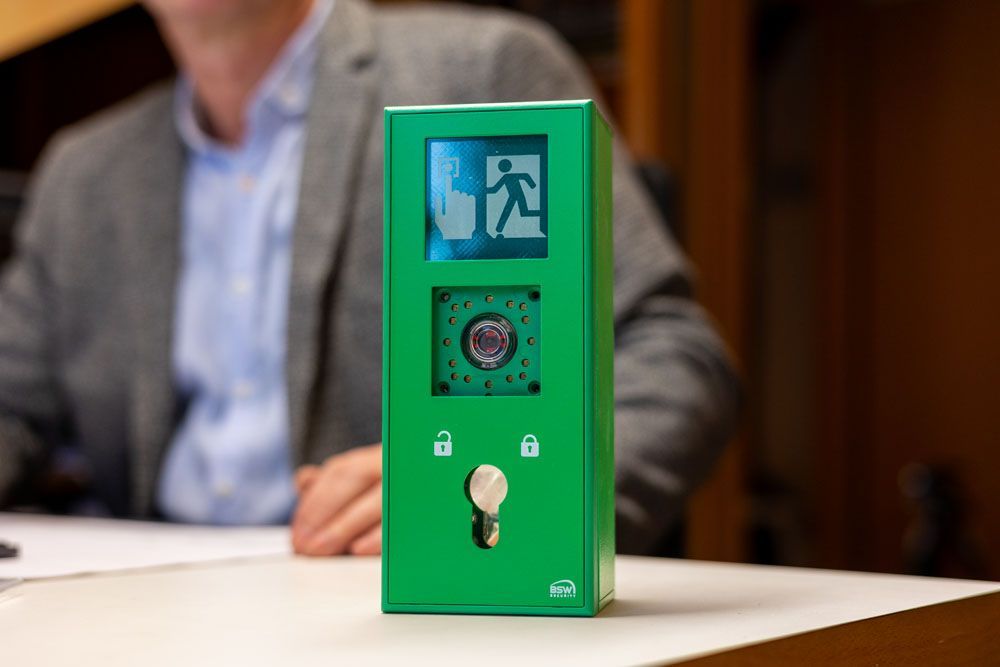 Ein Mann im Anzug sitzt an einem Tisch, auf dem ein grünes Gerät liegt