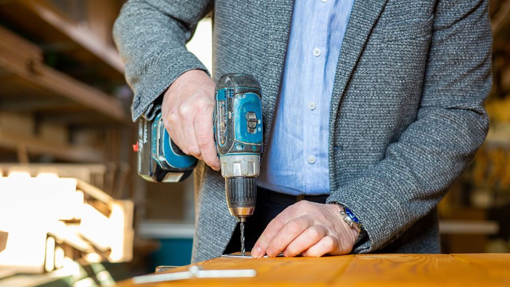 Ein Mann bohrt mit einem Bohrer ein Loch in ein Stück Holz.