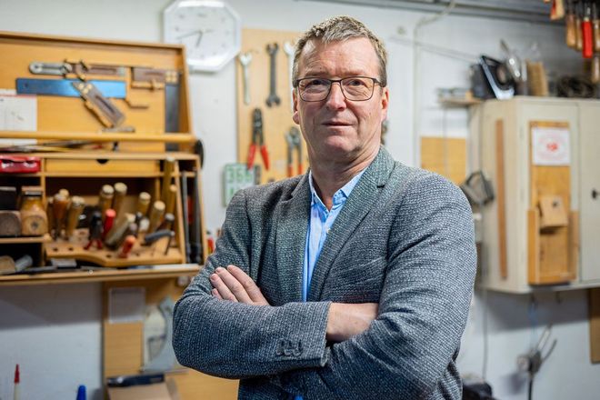 Ein Mann in Anzug und Brille steht mit verschränkten Armen in einer Werkstatt.