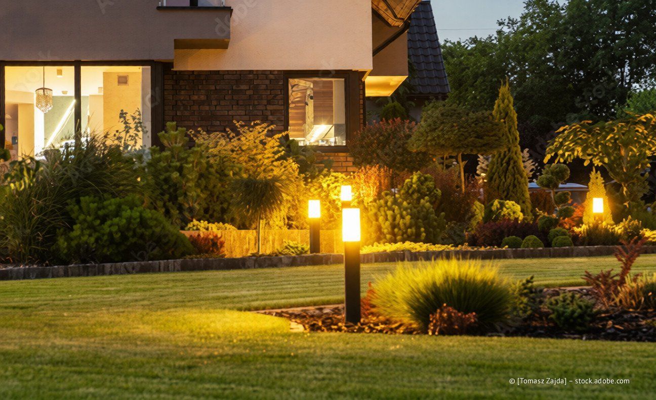 Gut beleuchteter Rasen mit Garten und modernem Haus im Hintergrund. Leuchtende Wegbeleuchtung.