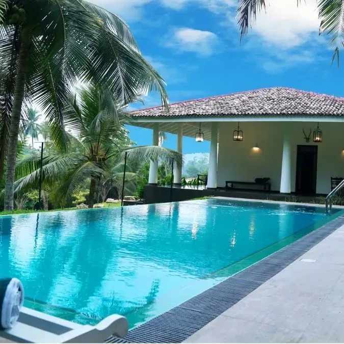 Piscina frente a una villa blanca con palmeras y un cielo azul brillante.