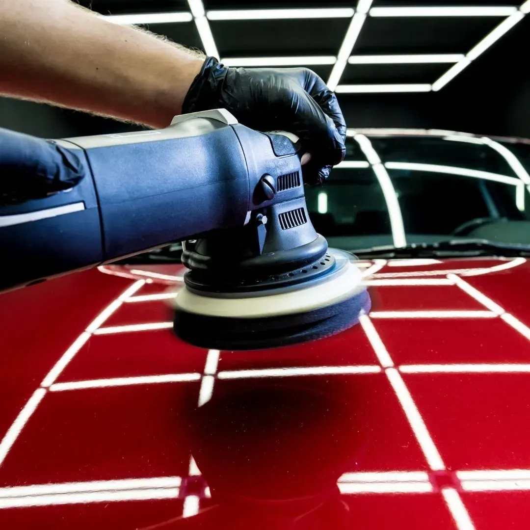 Puliendo a mano un coche rojo con una pulidora eléctrica en un garaje bien iluminado.