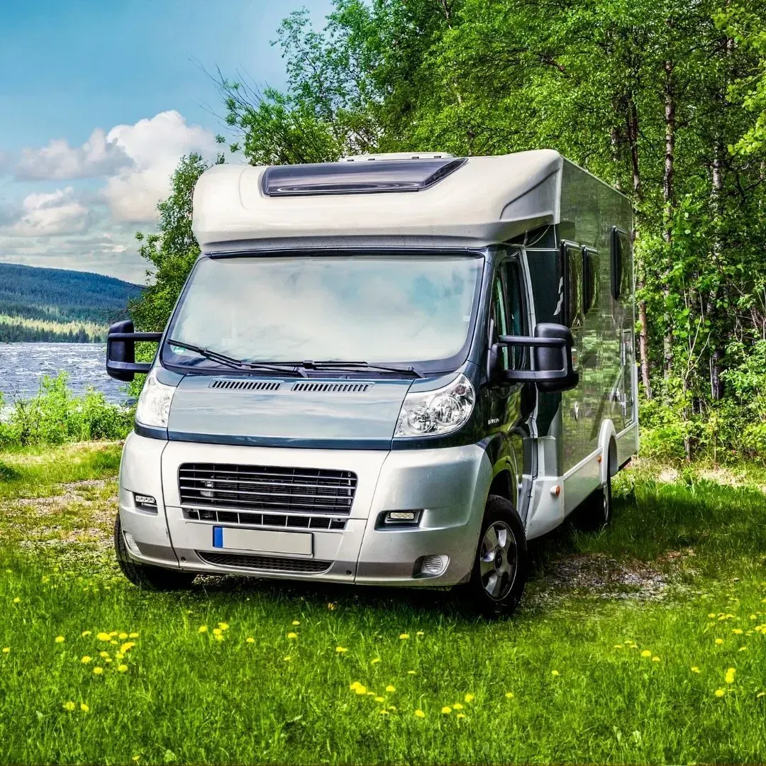 Casa rodante estacionada en una zona verde, con un lago y árboles al fondo.