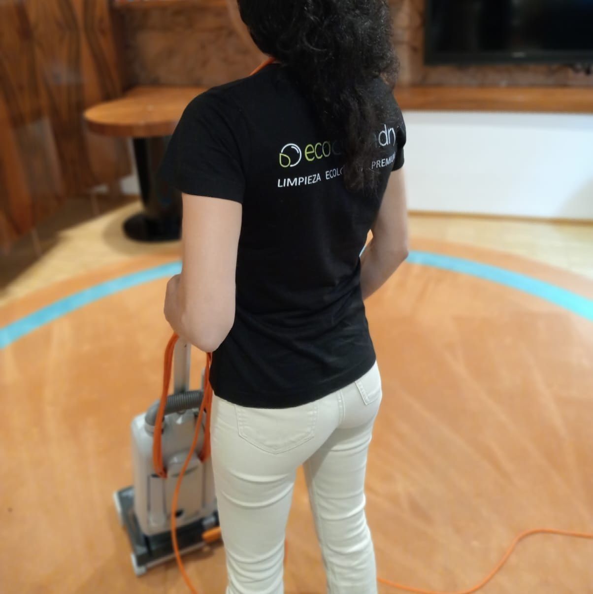 Persona con camisa negra y pantalón blanco operando máquina limpiadora de pisos en un piso circular.