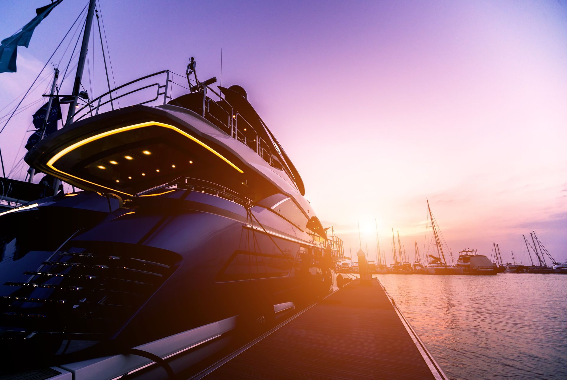 Yate de lujo atracado en un puerto al atardecer, con cielo violeta y naranja.