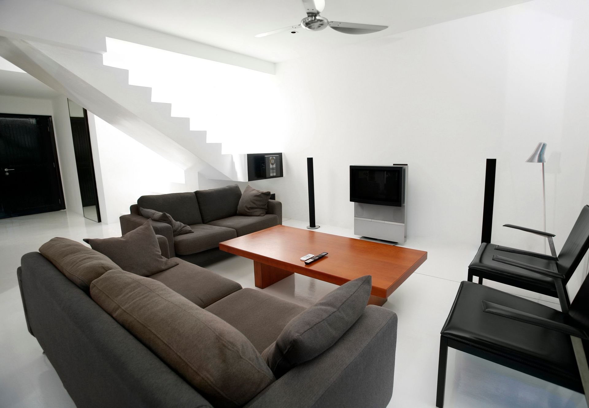 Sala de estar moderna con paredes blancas, sofá seccional gris, mesa de centro de madera y sillas negras.