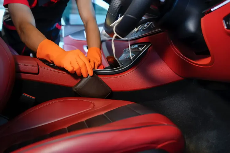 Persona con guantes naranjas limpiando el interior de un coche rojo con una herramienta.