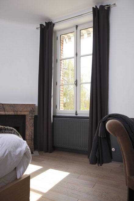 Chambre avec fenêtre, rideaux gris foncé, murs blancs et vue sur les arbres.