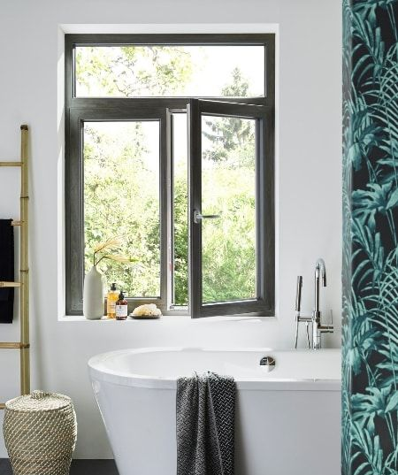 Salle de bains avec baignoire blanche sous une fenêtre à cadre sombre.