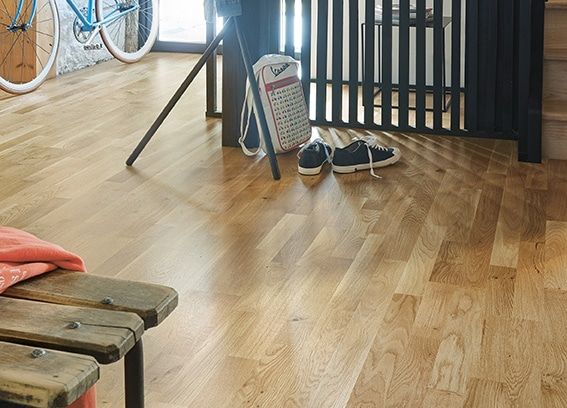 Une pièce avec un parquet, un banc en bois, des chaussures et une balance ancienne.