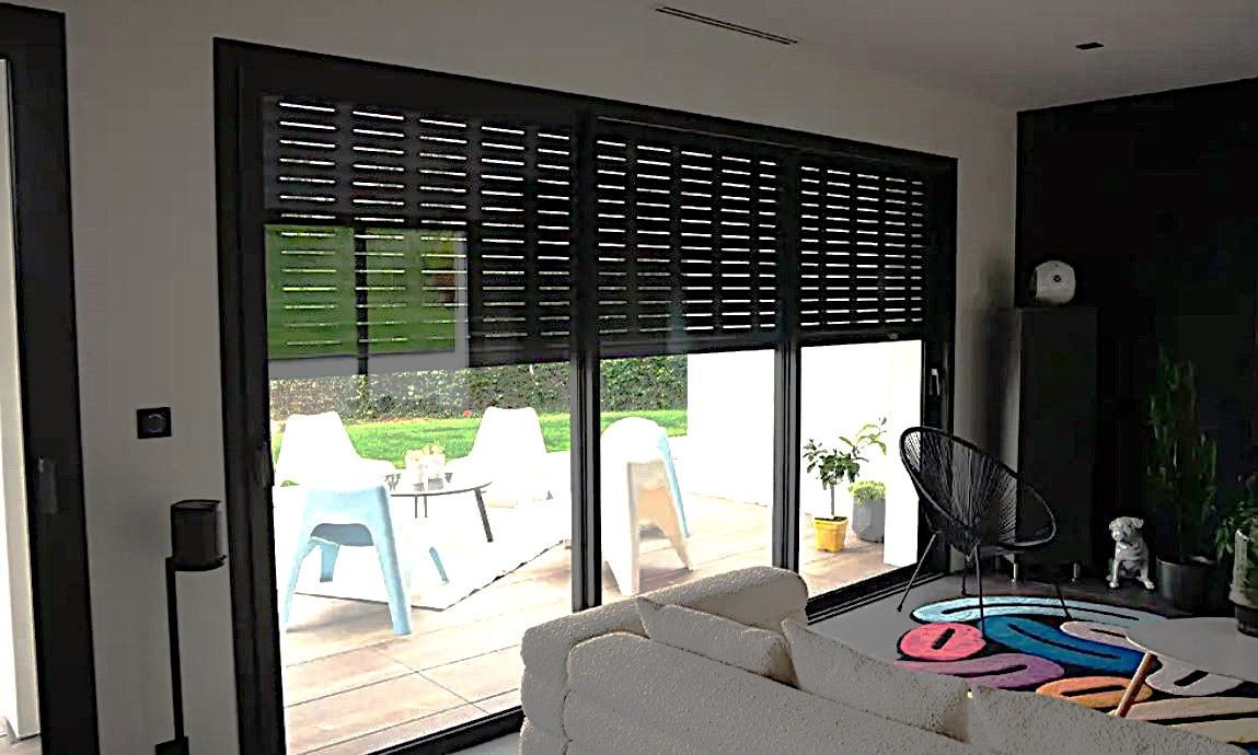 Des volets roulants noirs recouvrent une porte coulissante en verre, laissant entrevoir un espace de vie intérieur.