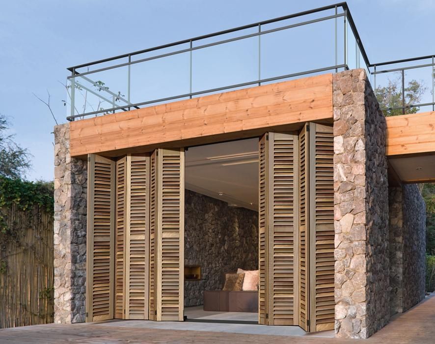 Bâtiment en pierre et en bois, avec des volets en bois pliants ouverts dévoilant un coin salon intérieur.
