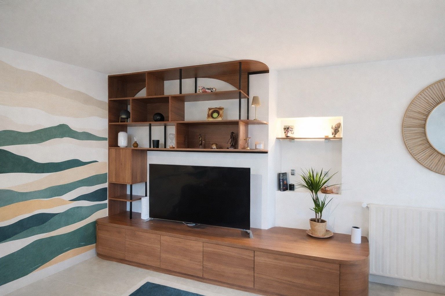 Meuble TV en bois avec télévision, étagères et rangements, fixé sur un mur blanc orné d'œuvres d'art et d'un miroir rond.