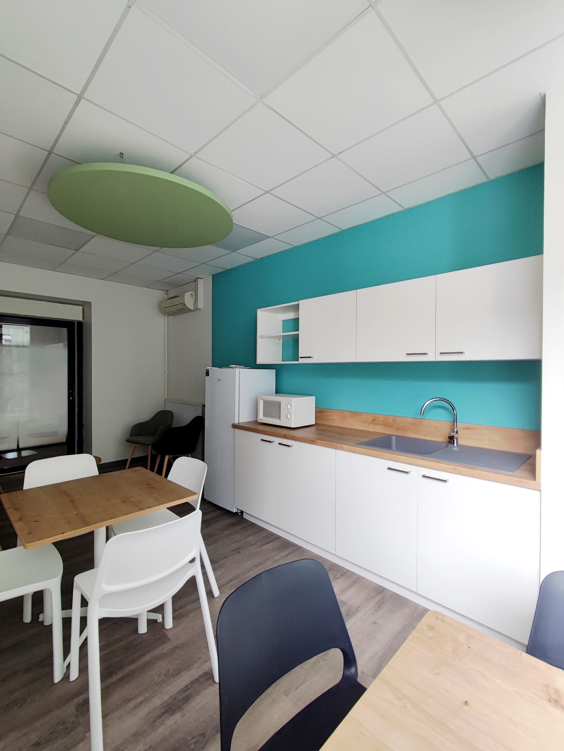 Coin cuisine avec placards blancs, mur turquoise et table avec chaises.