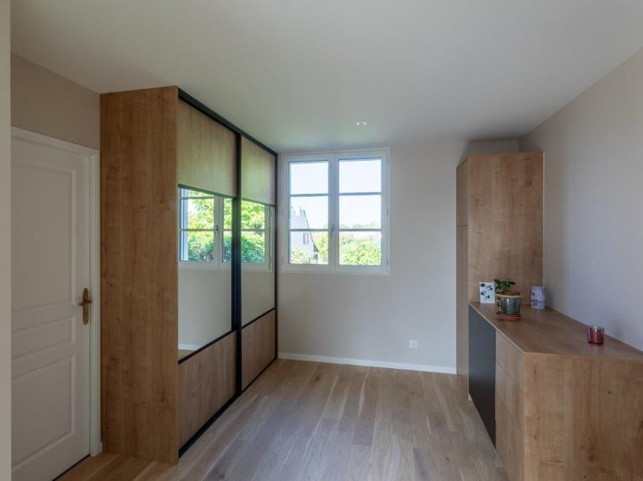 Chambre avec armoire à portes coulissantes en bois, fenêtre, bureau et parquet.