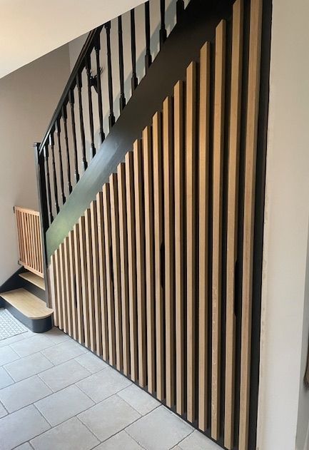 Escalier avec rampe noire et lambris en lattes de bois. Sol carrelé clair.
