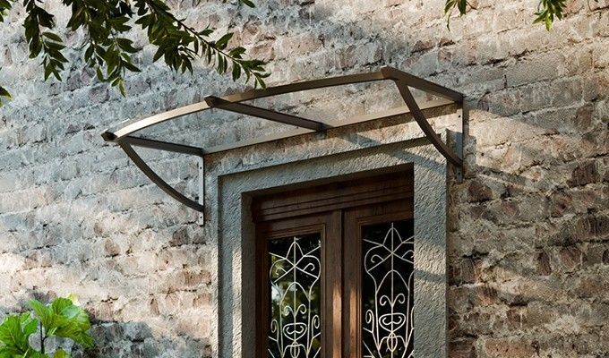 Auvent au-dessus d'une fenêtre. Une structure métallique soutient un toit transparent et incurvé.