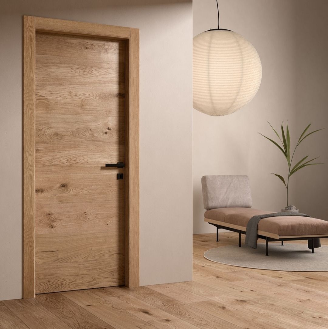 Porte en bois dans une pièce aux tons neutres avec une poignée noire, une méridienne et une suspension décorative.
