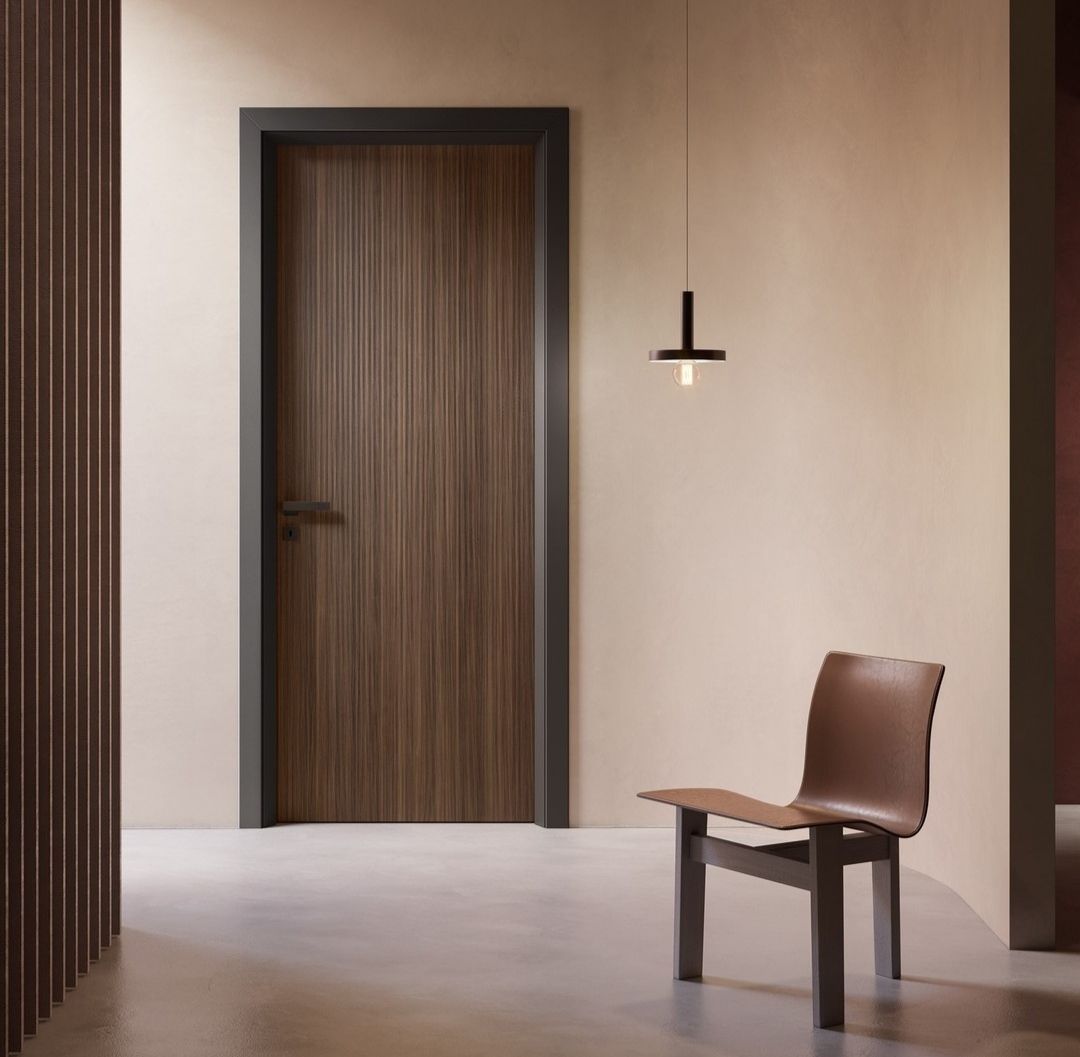 Porte en bois brun avec cadre foncé, chaise et suspension lumineuse dans un couloir aux tons neutres.