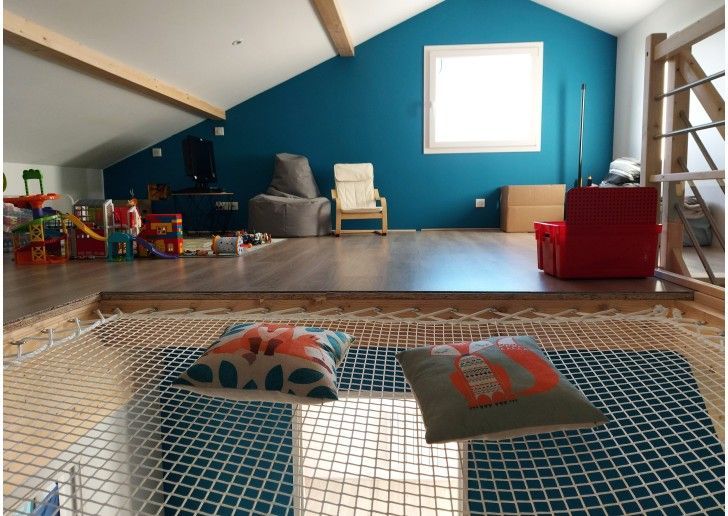 Salle de jeux en mezzanine avec parquet, hamac en filet avec coussins et mur bleu.