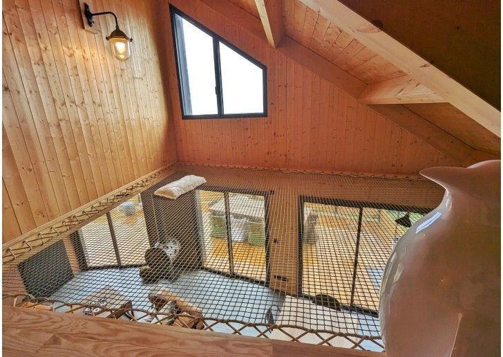 Pièce mansardée en bois avec plancher en filet, fenêtres et plafond en pente.