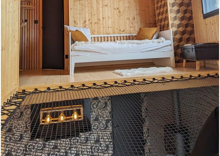 Chambre en mezzanine avec un lit, des lambris et un plancher en filet au-dessus d'une zone inférieure.