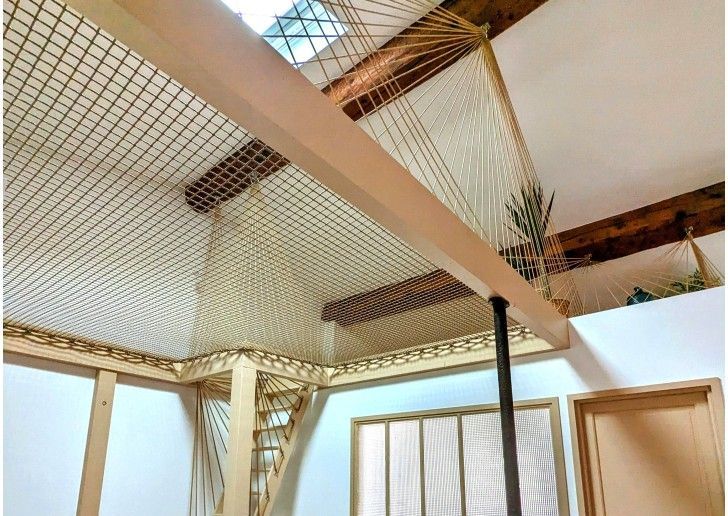 Vue intérieure d'une pièce avec une poutre en bois, un plafond en filet tissé et des murs blancs.