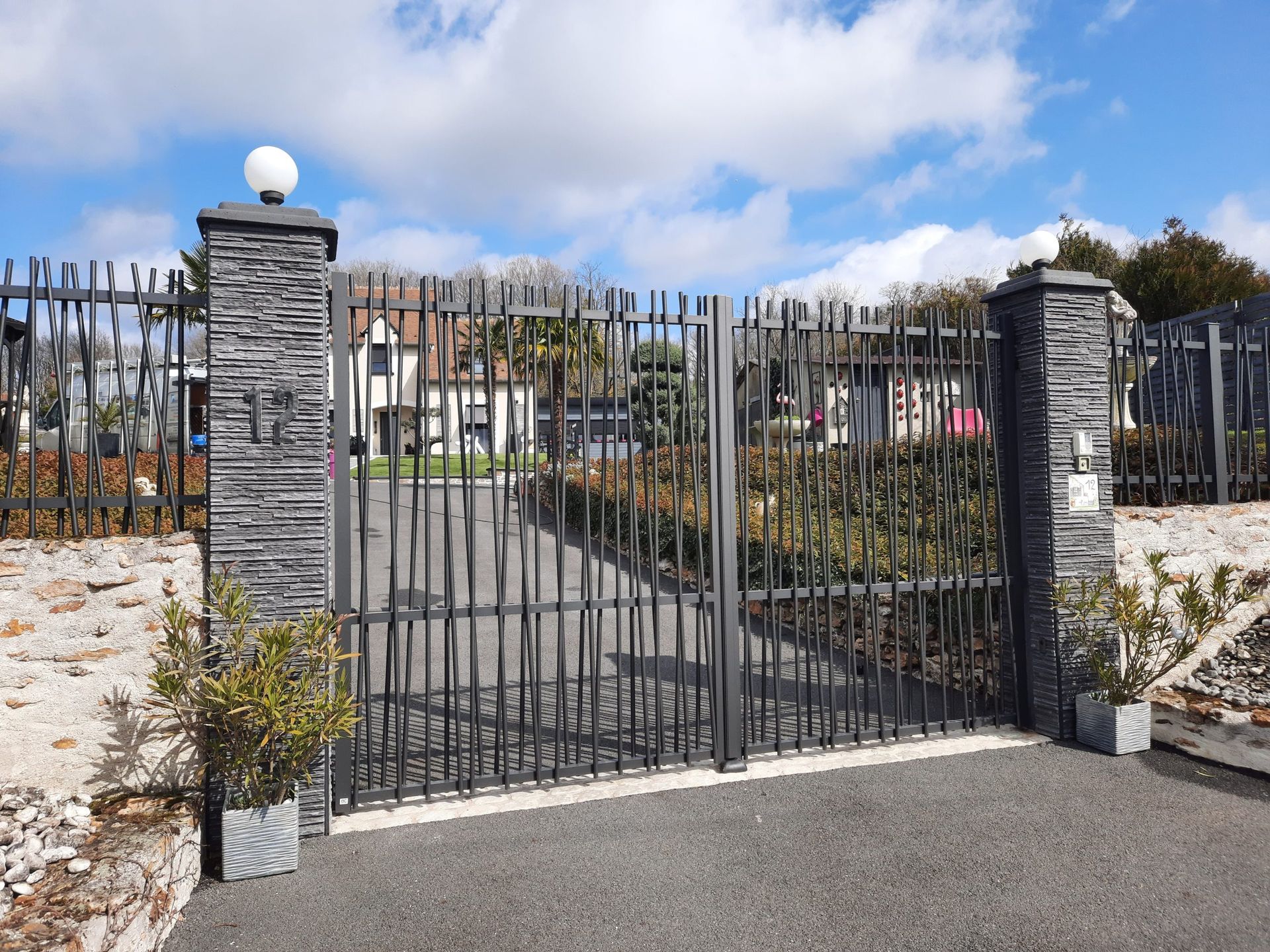 Portail et clôture en métal noir, avec des colonnes en pierre, menant à une allée.