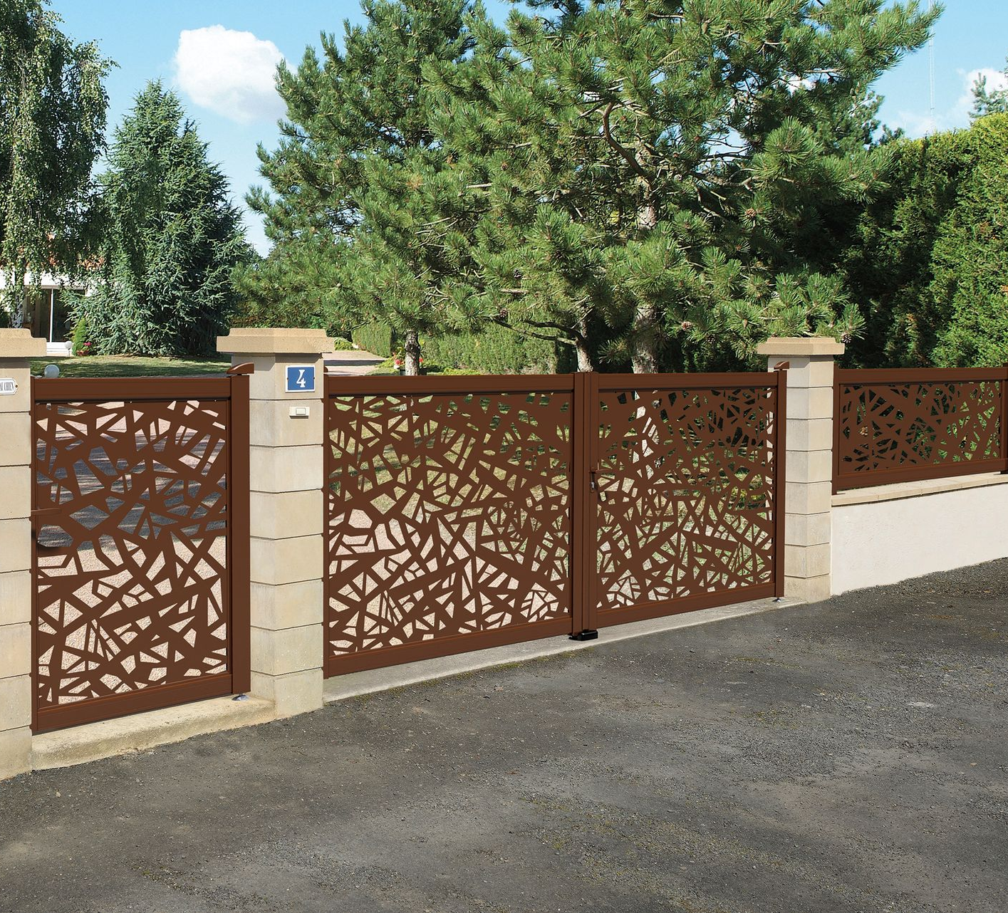 Portail et clôture décoratifs en métal marron avec piliers en pierre beige devant une maison.