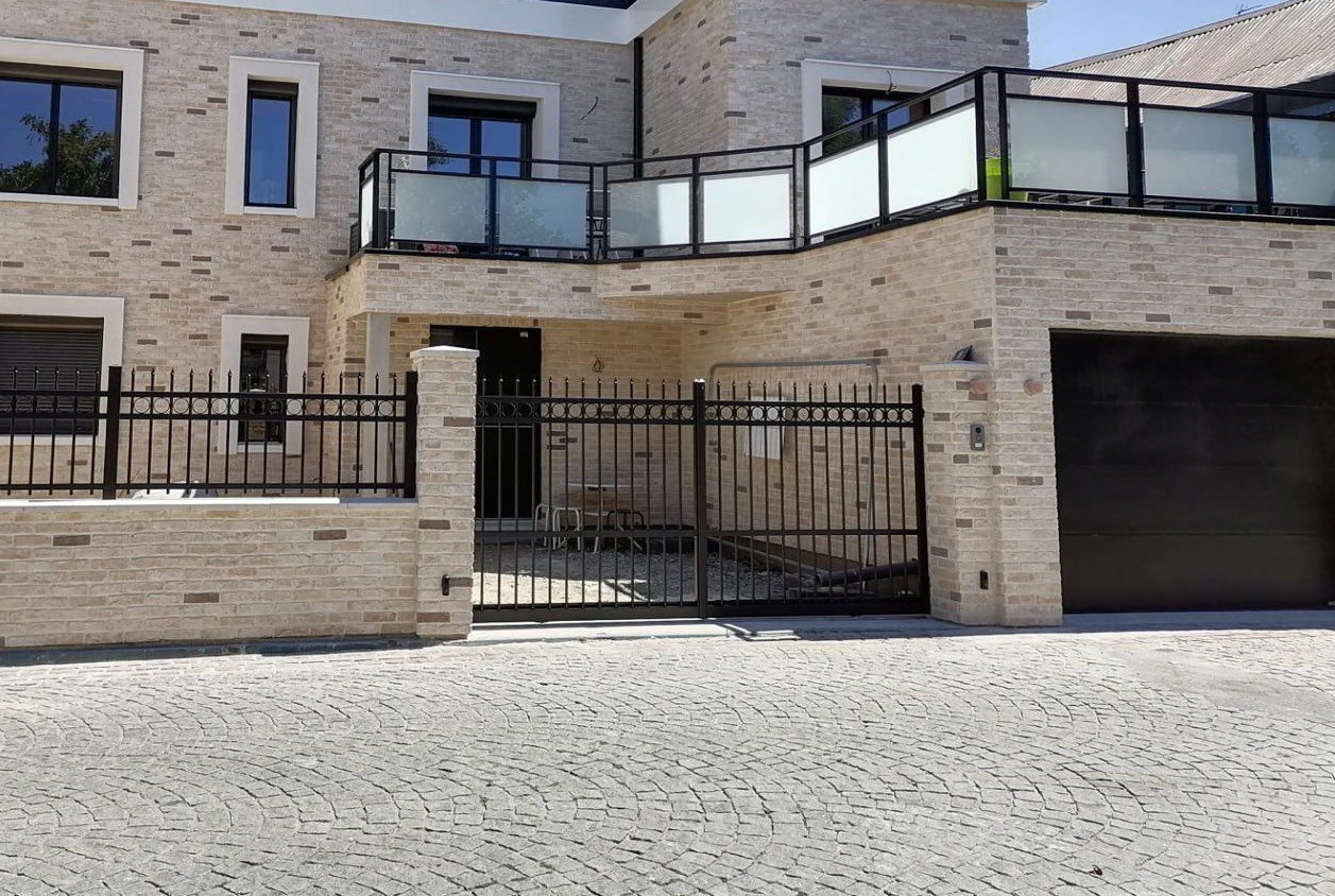 Maison en briques avec clôture et portail en fer forgé noir, allée pavée.
