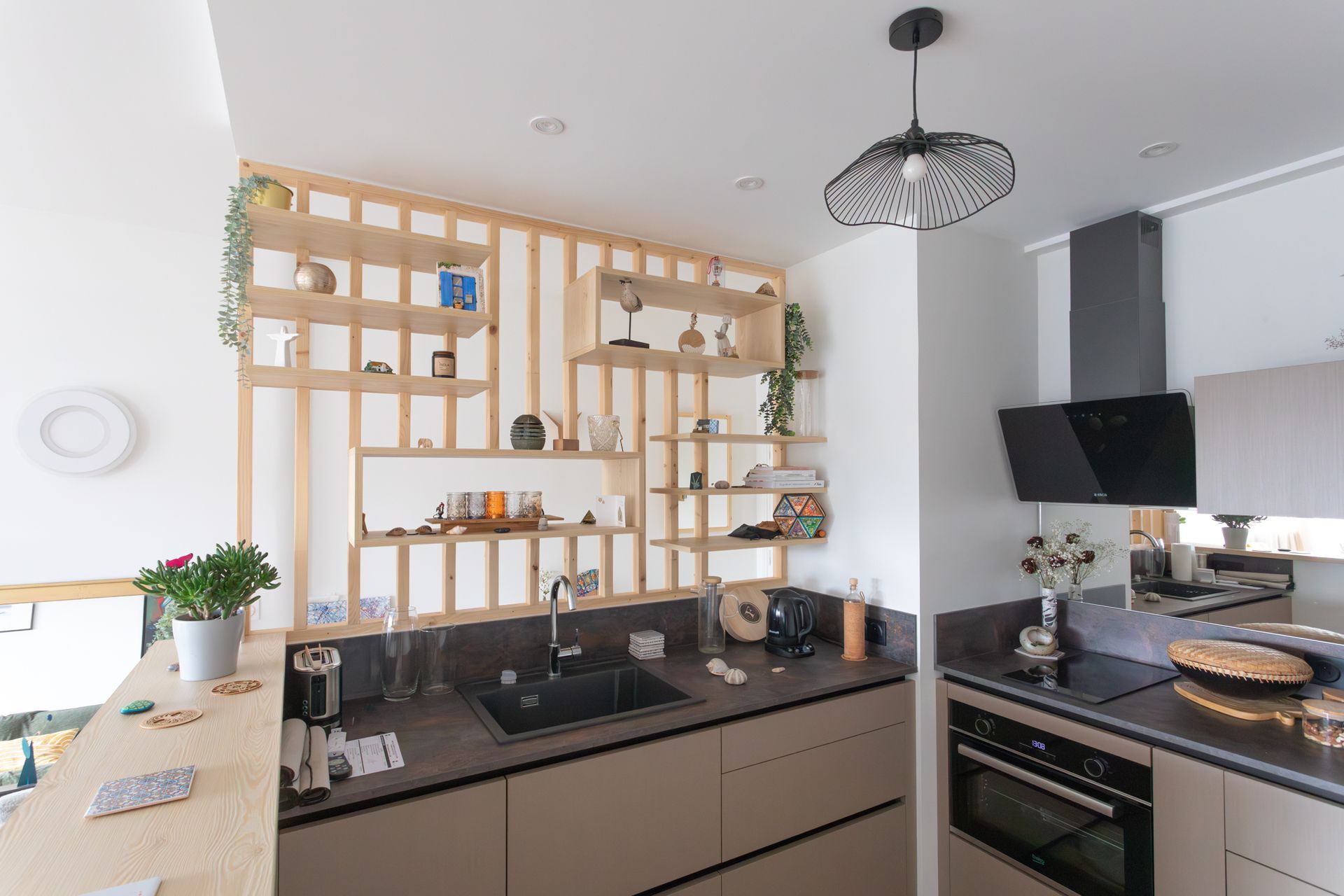 Cuisine moderne avec étagères en bois clair, plans de travail foncés, évier et appareils électroménagers noirs.