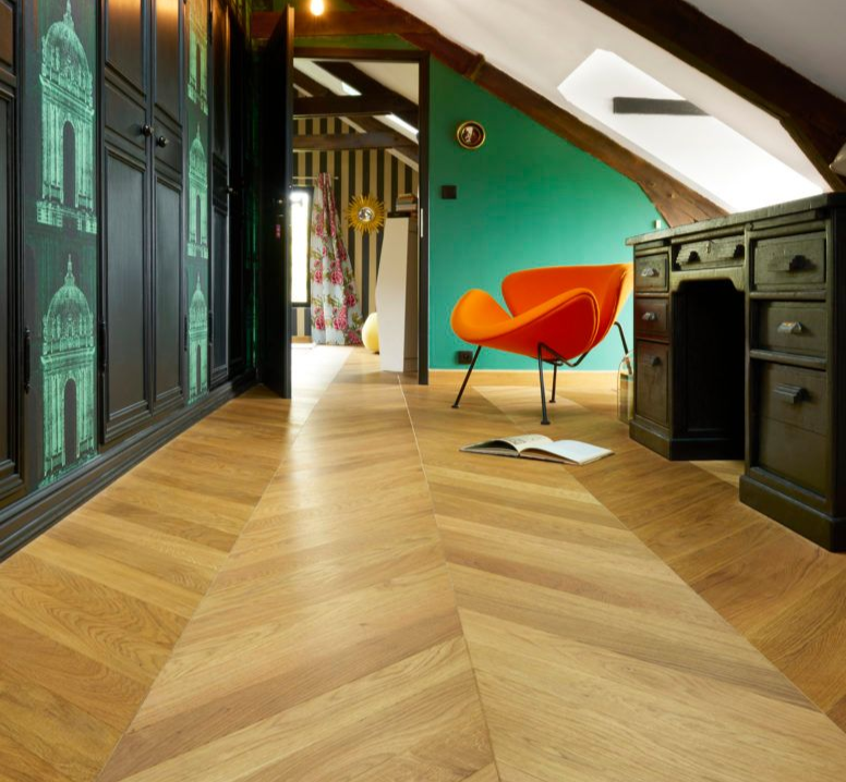 Un sol en parquet à chevrons dans une pièce avec un bureau noir, une chaise orange et un mur d'accent vert.