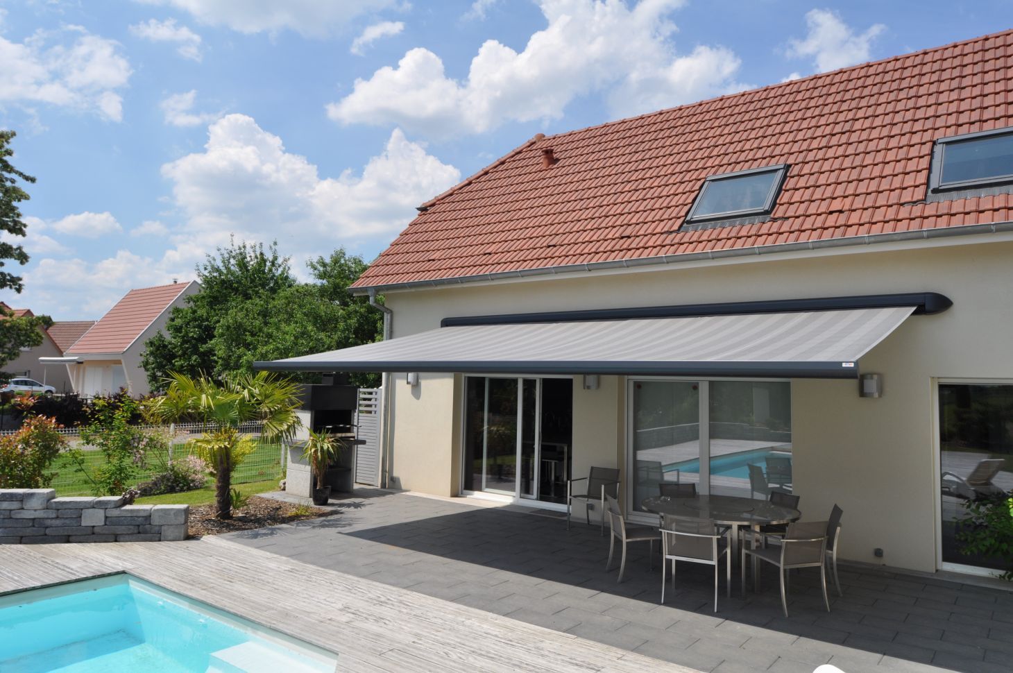 Store électrique d'une couleur gris au-dessus d'une terrasse et devant une piscine