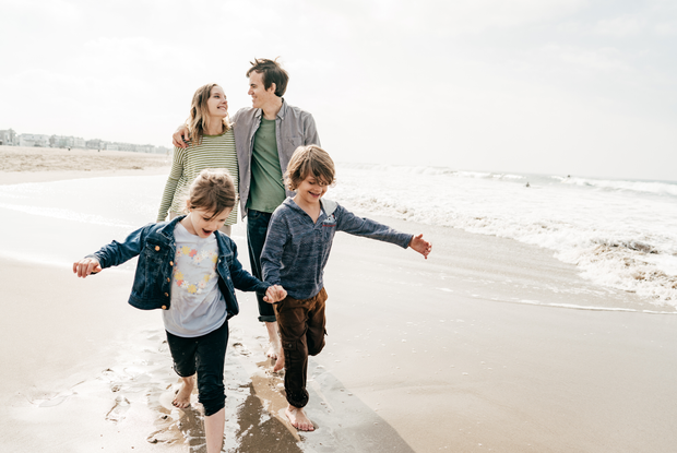 Una famiglia cammina sulla spiaggia tenendosi per mano.