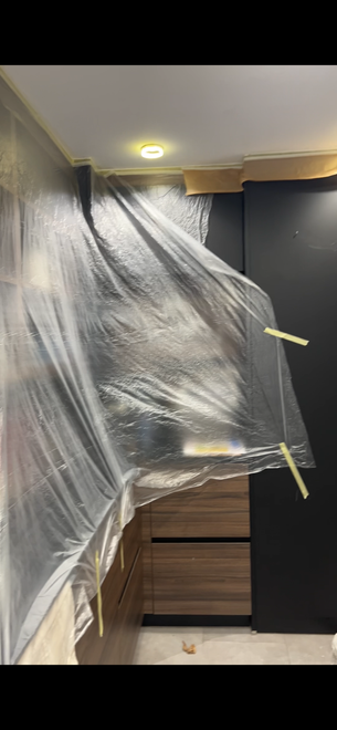 Plástico sujeto con cinta sobre una puerta en una habitación en obras, con una cómoda y una pared oscura cerca