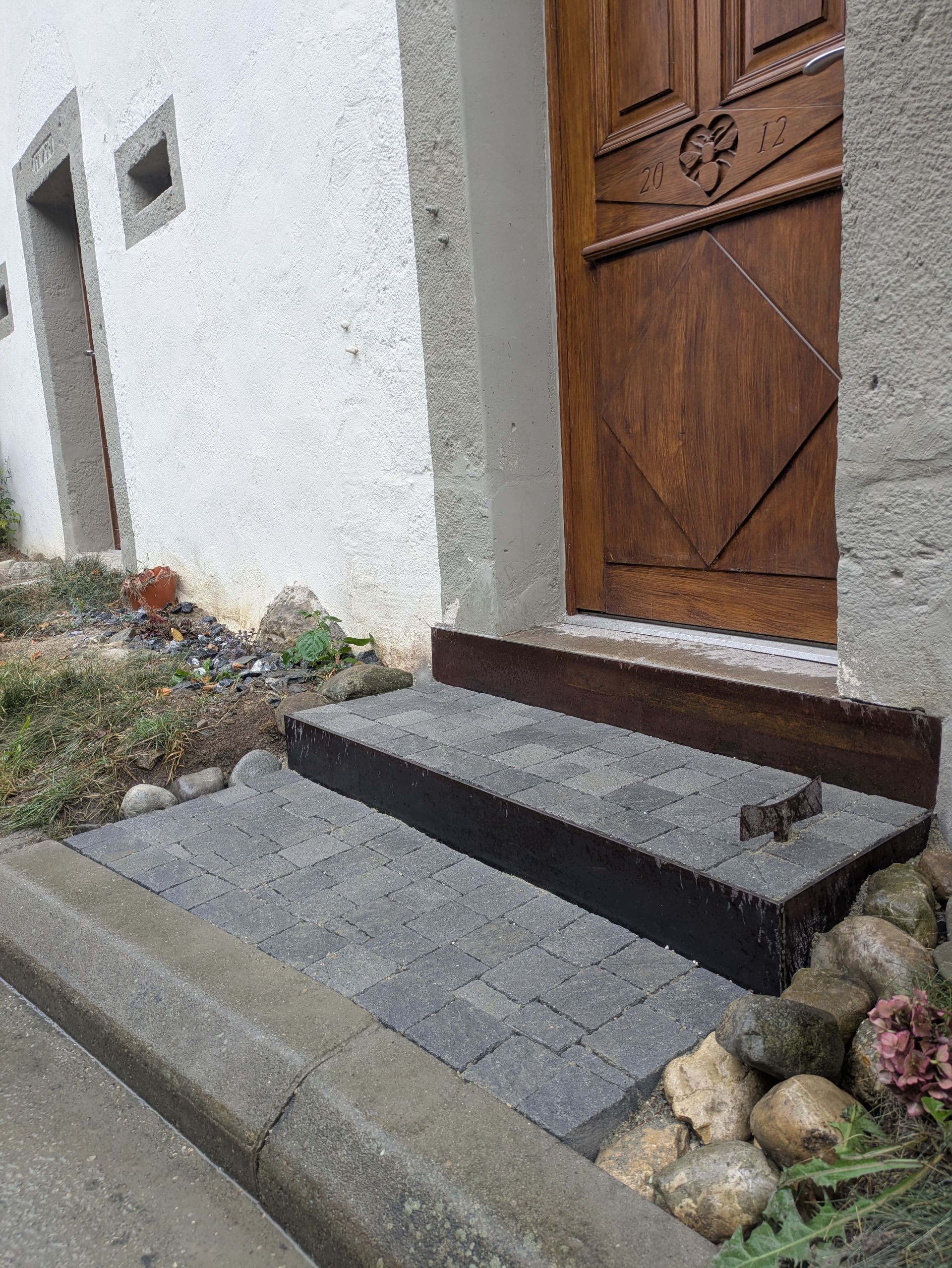 Extérieur : Marches menant à une porte en bois. Les marches sont pavées gris foncé, avec une bordure gris clair