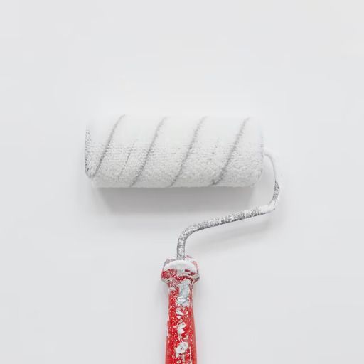 Un rodillo de pintura blanco con mango rojo sobre una pared blanca.