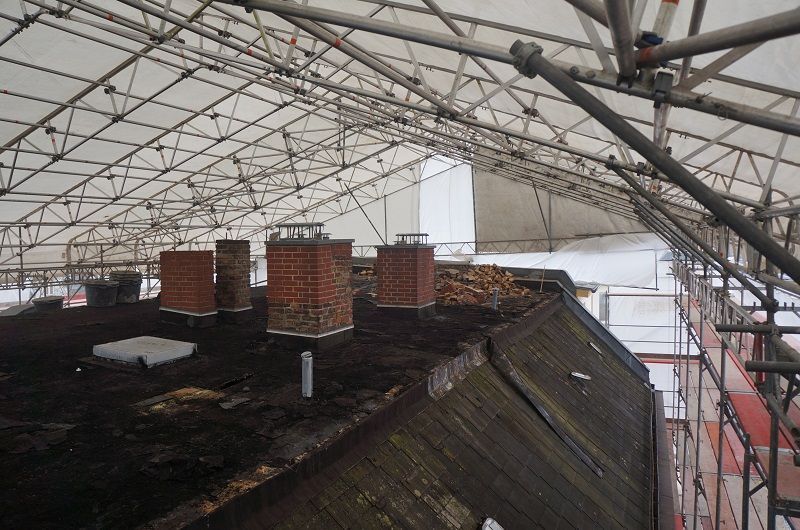 Das Dach eines Gebäudes ist mit Gerüsten und Schornsteinen bedeckt.