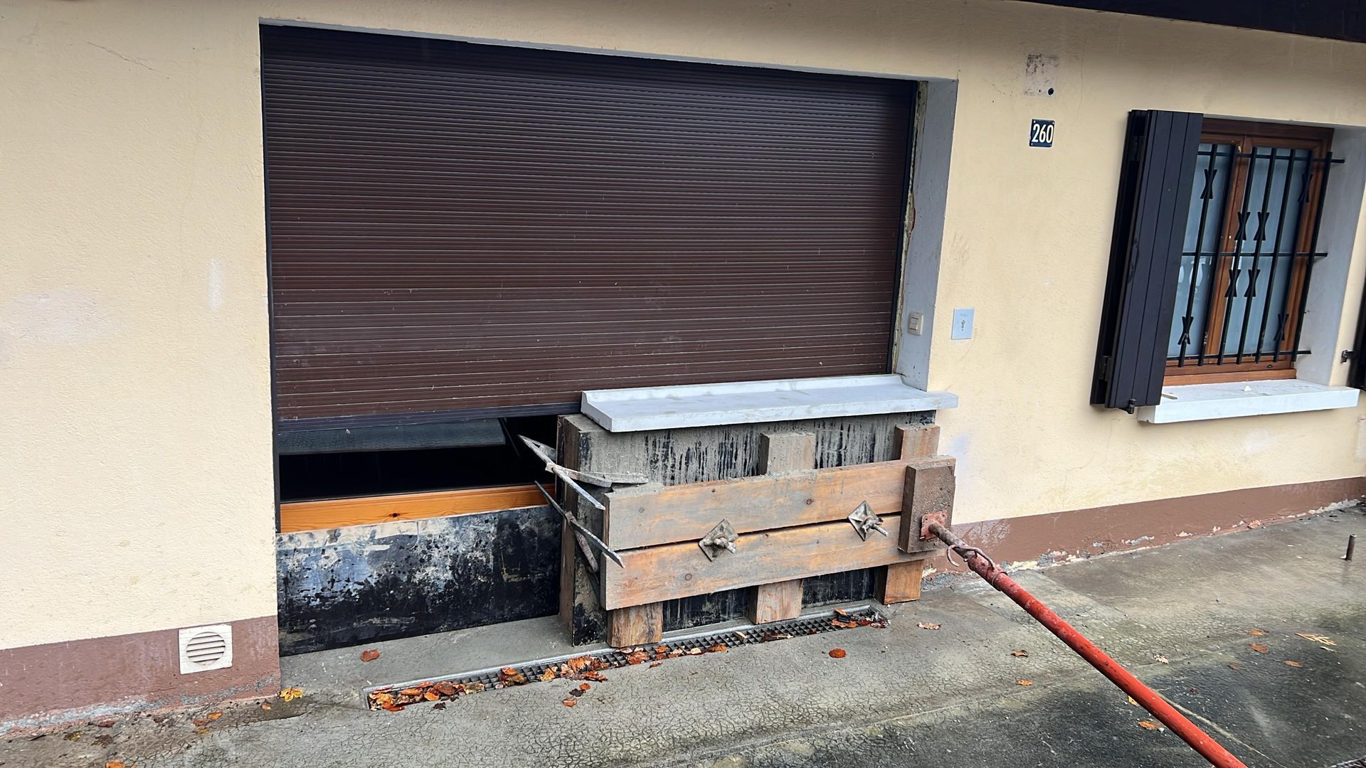 L'entrée d'un garage est partiellement obstruée par une structure en palettes de bois maintenue en place par un poteau de soutien métallique.