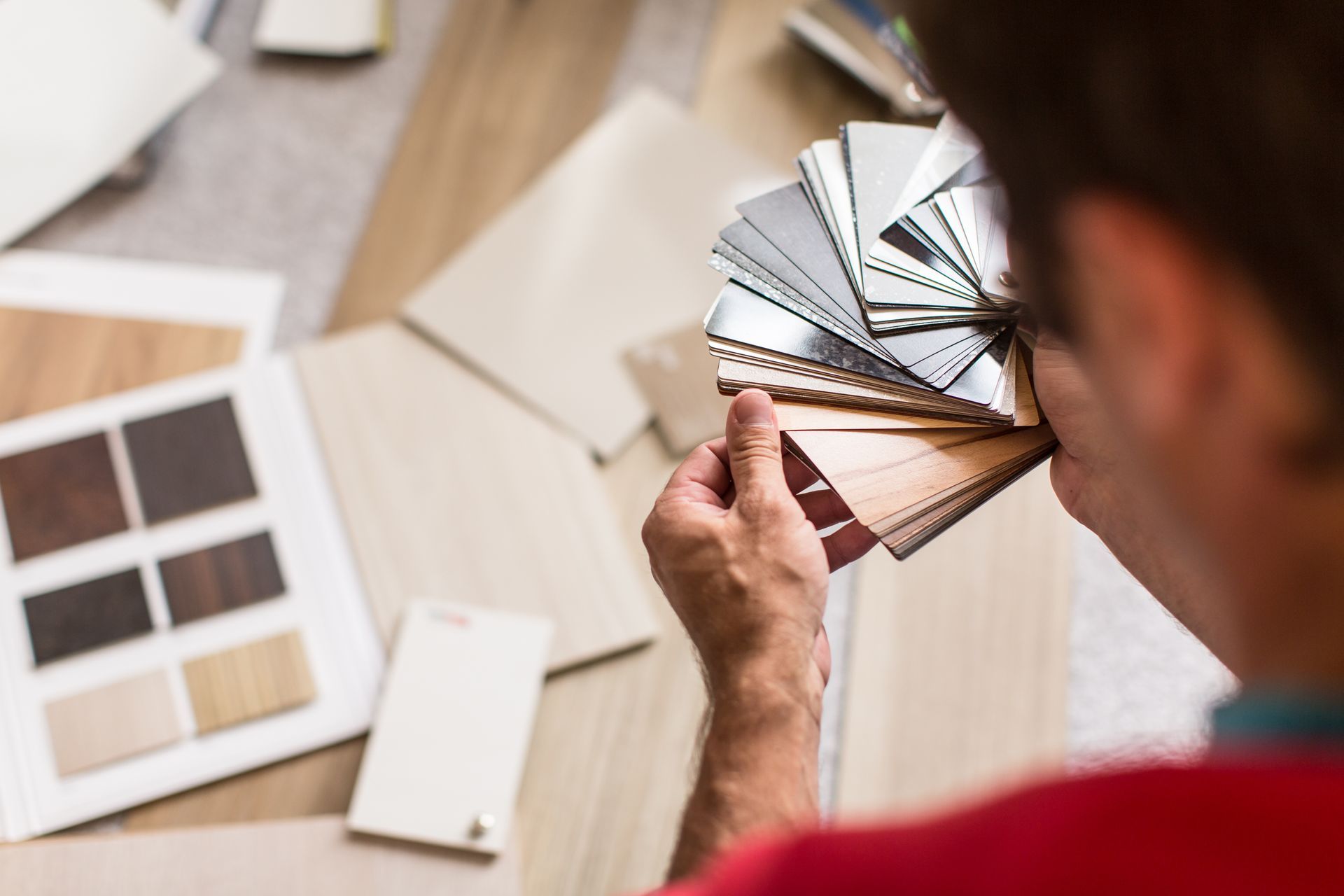 Une personne tient un éventail d'échantillons de matières et de couleurs variées tout en évaluant des échantillons étalés sur une surface de travail.