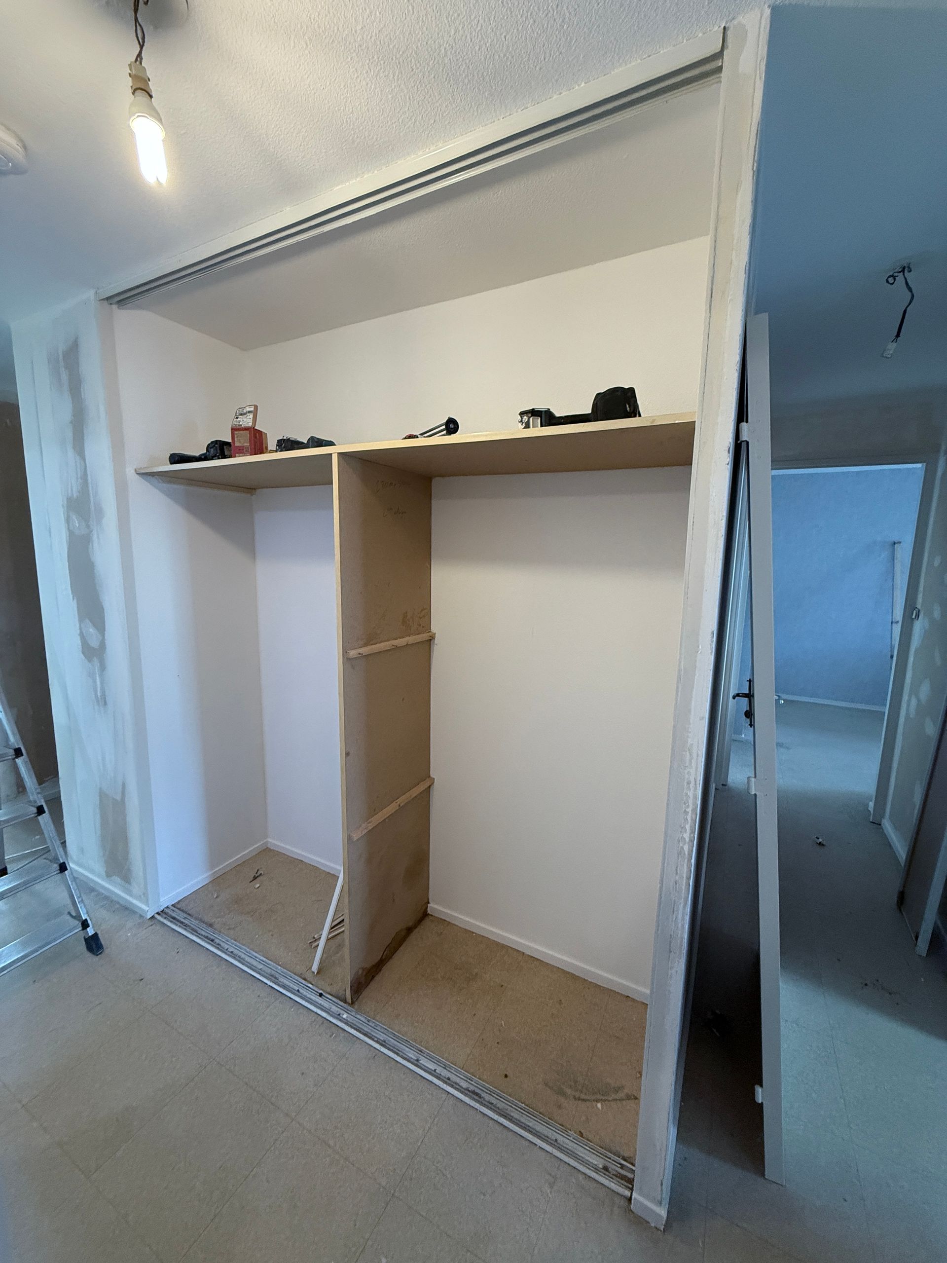 Une structure de placard en bois avec une étagère supérieure en cours de construction, installée dans une pièce aux murs non finis et avec un rail au sol.