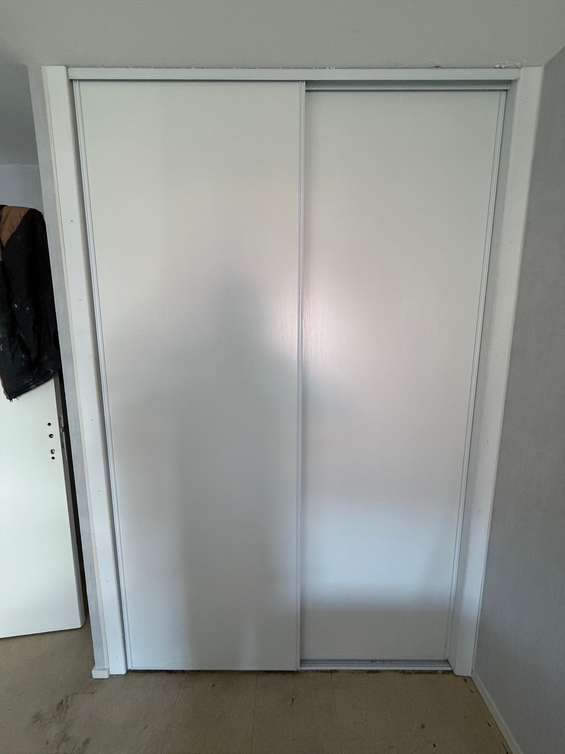 Deux portes de placard coulissantes blanches et lisses, installées dans une chambre résidentielle.