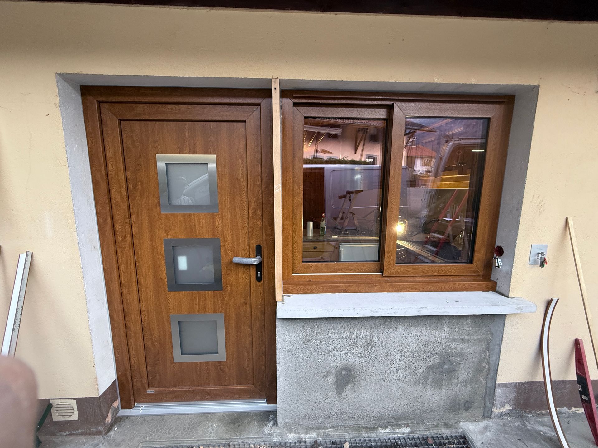 Une porte d'entrée en bois brun avec trois panneaux de verre carrés, jouxtant une fenêtre assortie au-dessus d'un mur revêtu de pierre.