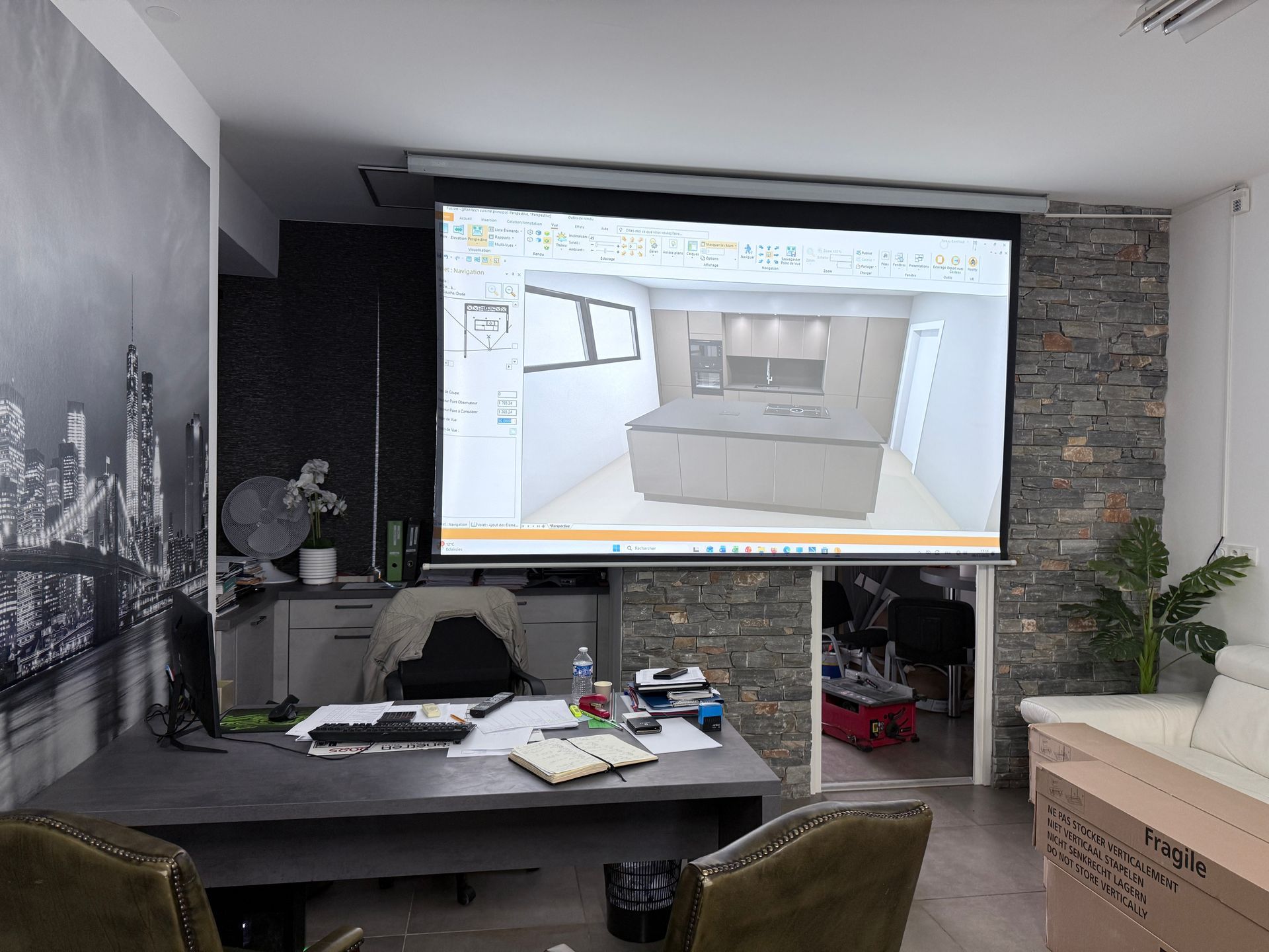 Un bureau d'études doté d'un grand écran de projection affichant une modélisation 3D d'une cuisine, d'un bureau et d'éléments muraux en pierre.