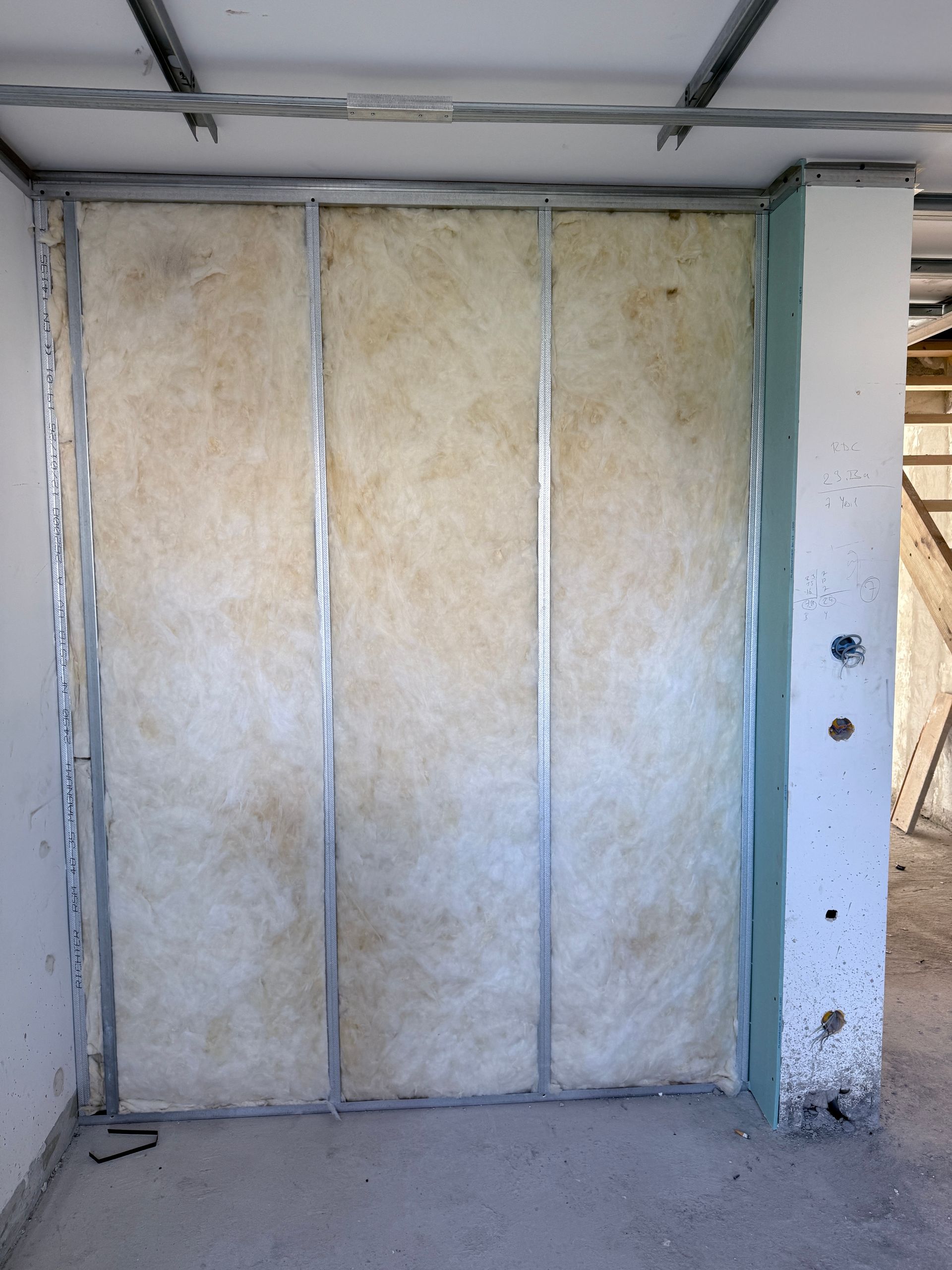 Ossature murale intérieure avec montants métalliques et isolation en laine de verre jaune en cours de construction.