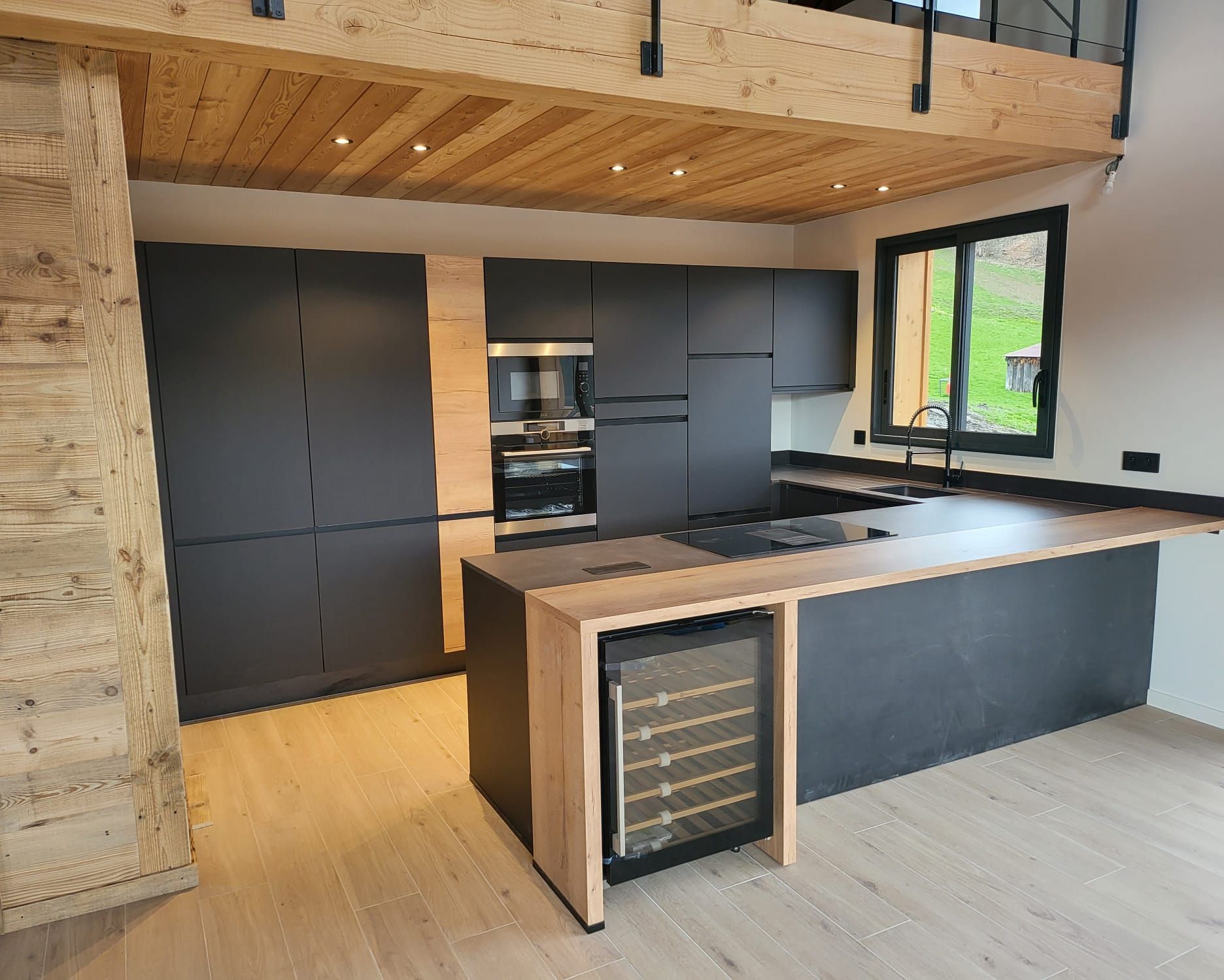 Une cuisine moderne avec des armoires noires mates, des touches de bois clair, une cave à vin intégrée et un plafond en bois surélevé.