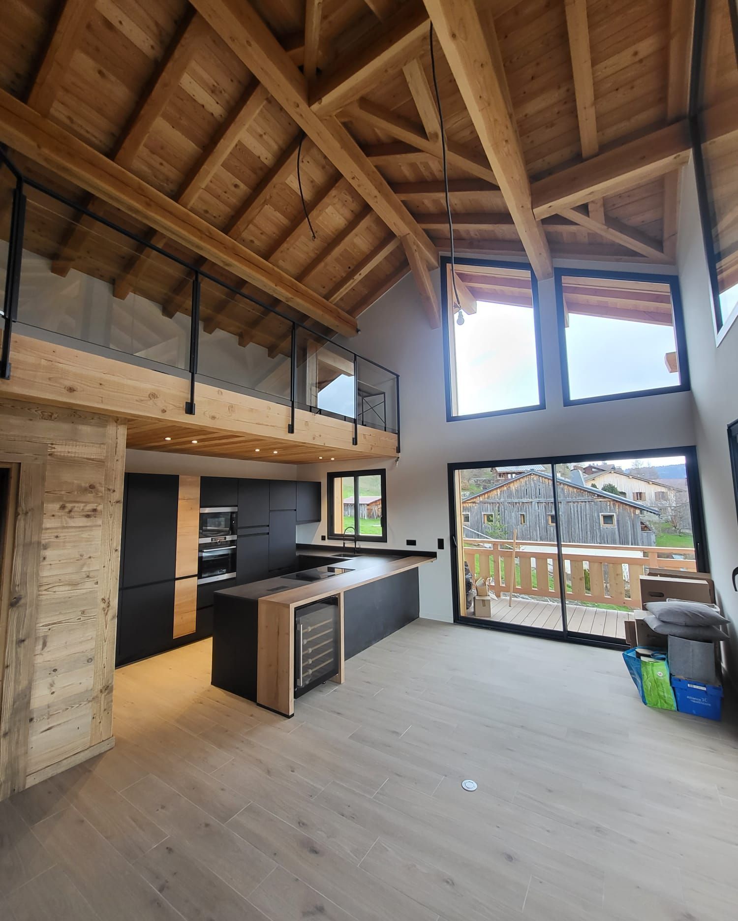 Intérieur de chalet moderne avec un plafond voûté en bois, une mezzanine et une cuisine équipée de placards noirs et d'un îlot central.