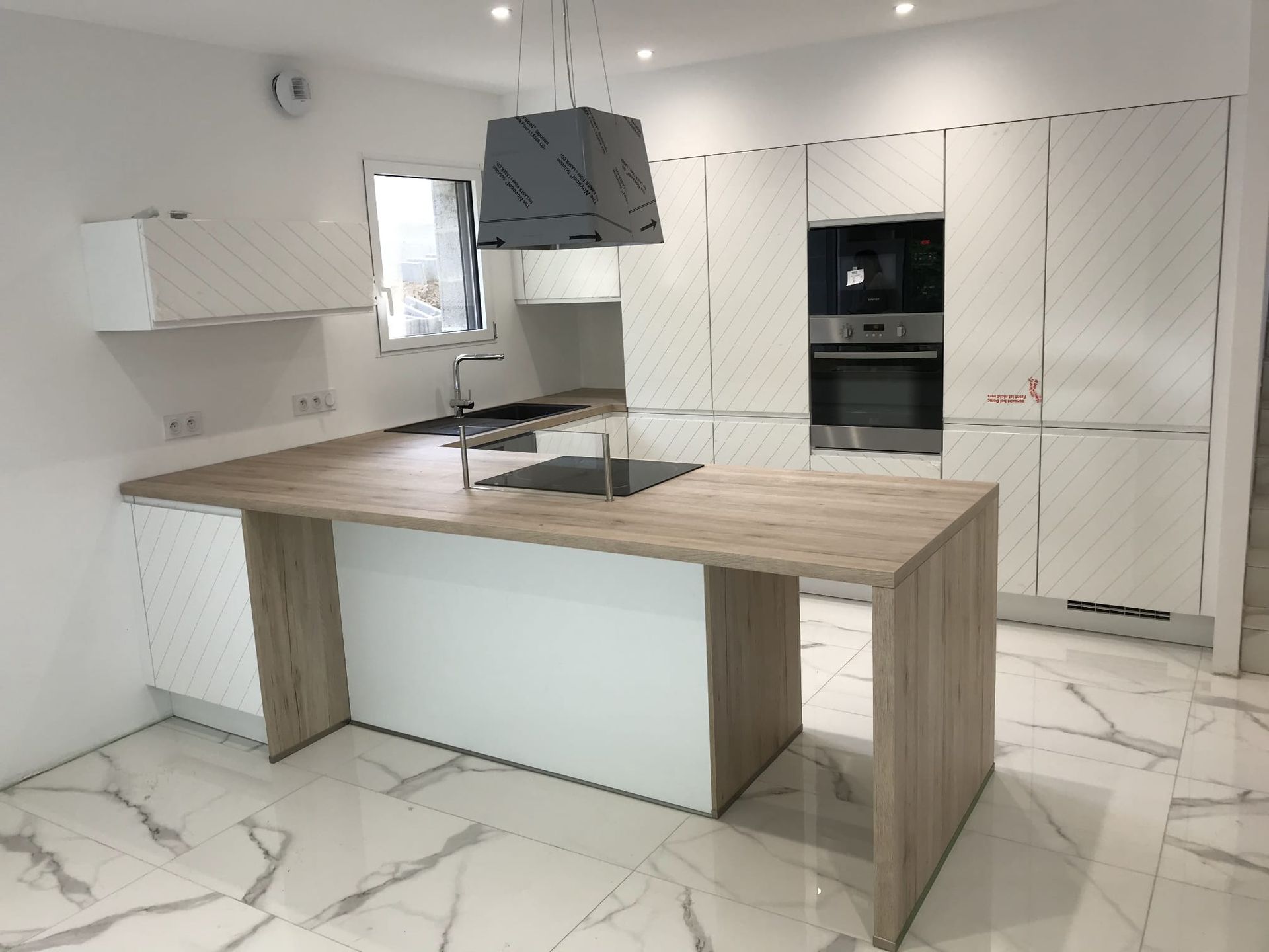 Cuisine moderne blanche avec un îlot central au comptoir en bois, un four en acier inoxydable et un sol en marbre blanc.